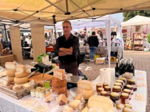 Un produttore dietro al proprio banco con formaggi e vasetti di miele durante la fiera