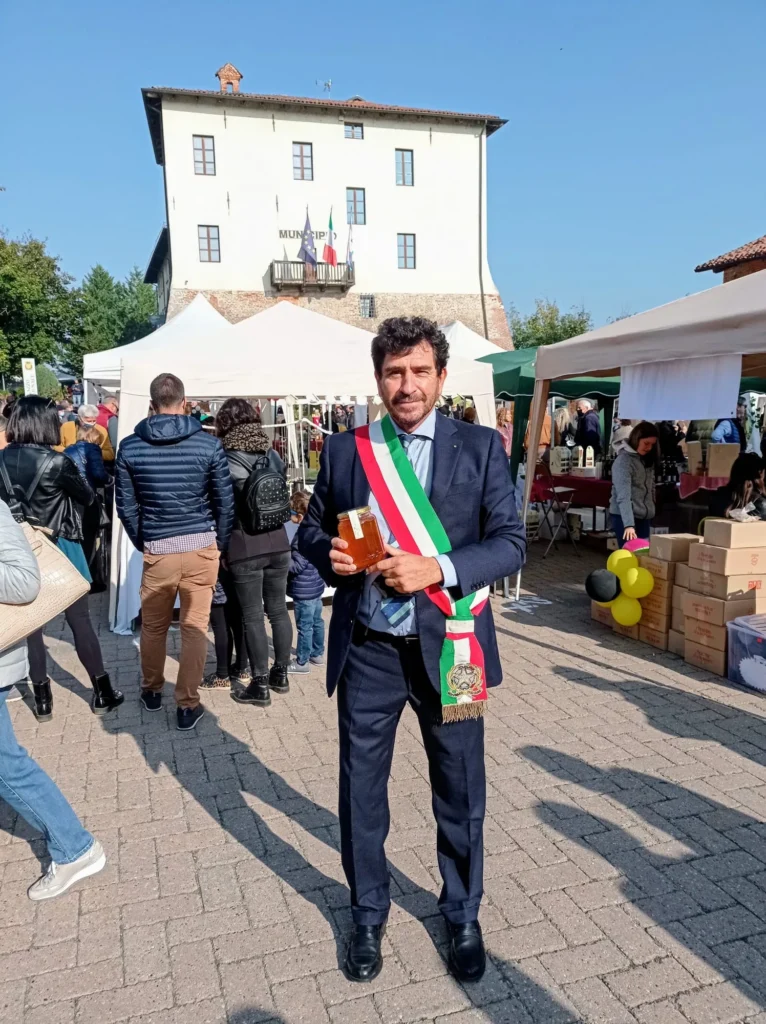 Il Sindaco di Ferrere Silvio Maria Tealdi con la fascia tricolore mostra un vasetto di miele davanti al Municipio durante la fiera
