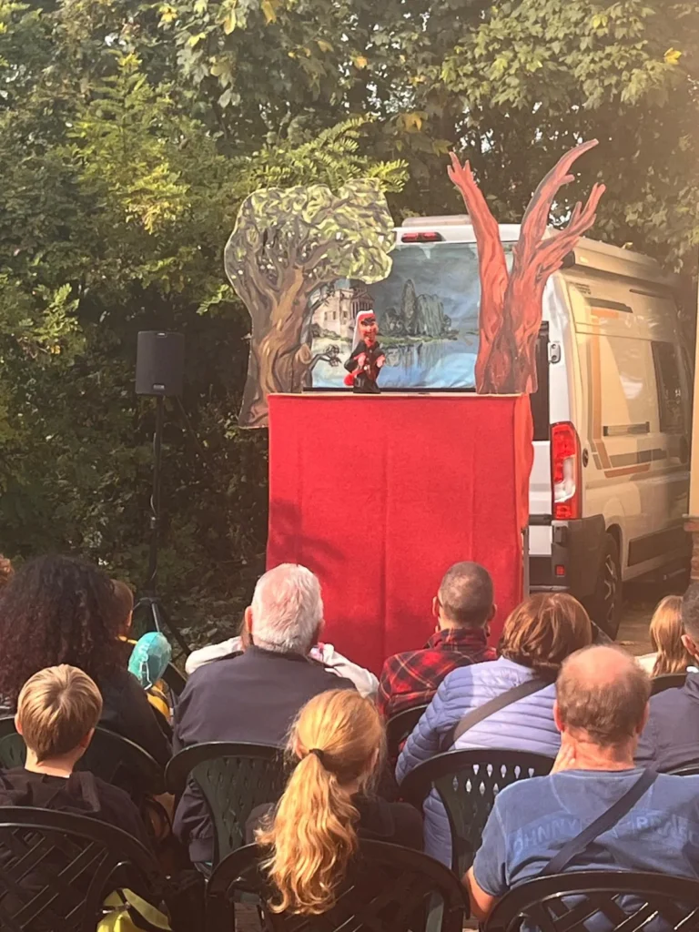 Spettacolo di marionette con sipario rosso e pubblico seduto all’aperto