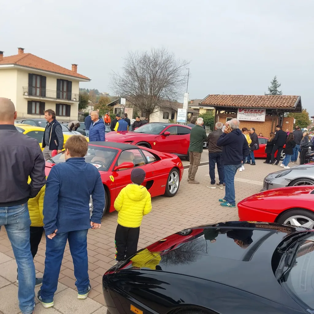 Bambini e visitatori intorno alle Ferrari rosse parcheggiate in piazza durante il raduno supercar
